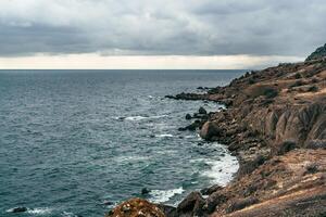 Coastal view with rocky shoreline and cloudy sky at the ocean's edge during late afternoon photo