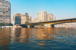 Cityscape view of a bridge spanning the Nile River with modern buildings along the waterfront in Cairo during a clear day photo
