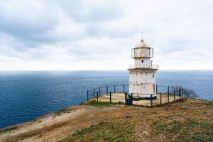 Lighthouse stands on cliff overlooking vast ocean under overcast sky at coastal location photo