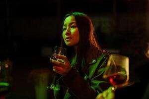 Woman enjoying a drink during a lively gathering in a dimly lit setting with vibrant green lights at night photo