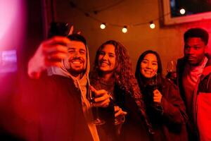 Group of friends enjoying a night out at a cozy bar, capturing memories with cheerful selfies while holding drinks photo
