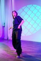 Performer demonstrates expressive dance movements under colorful lighting in a spacious studio setting photo