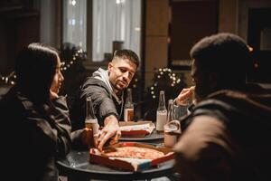Friends sharing pizza and drinks at night in a cozy outdoor setting with festive lights photo