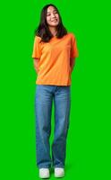 Smiling person stands confidently in orange shirt and blue jeans against a green background photo
