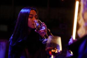 Woman enjoying a drink at a dimly lit bar during a night out with friends photo
