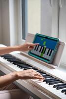 Young woman playing a keyboard while pointing at a learning app on a tablet. Technology enhances self-education in music, making learning more intuitive and engaging. High quality photo