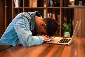 A tired student sleeping on the table while studying or working inside university library or office. photo
