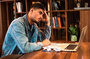 Tired male student crumples up the paper while studying inside university library. A stressed man working in the office or home workplace. photo