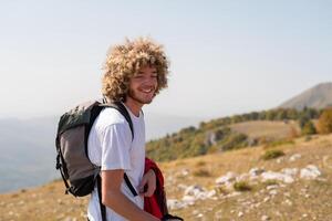 A young happy male traveler with curly hair enjoys while hiking or trekking trail mountain, active lifestyle. photo