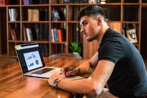 A male college student studying in a university library a young man working on laptop with graphs, charts, diagrams on screen in the office workplace. photo