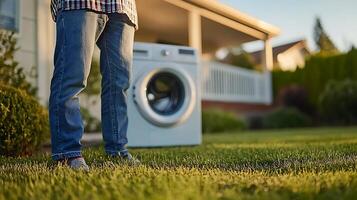 Man Standing on Grass Near a Washing Machine Outside a House. A view of a person's legs and feet in front of an appliance in a backyard setting. photo