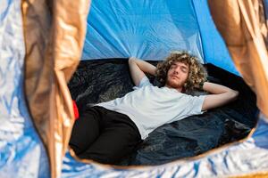 A young man lying with closed eyes in a camping tent. Happy sleeping. photo