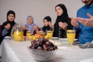 Happy Muslim family together making iftar dua to break fasting during Ramadan at home dining table at home focus on a bowl of dates healthy nutrition during the fast. photo