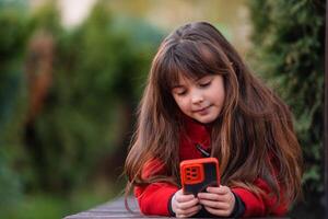 A happy child girl using a phone outside. photo