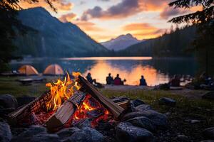 Campfire burning brightly at dusk near a lake with mountains and tents in the background scene photo