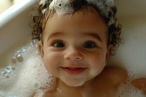 A happy baby with curly hair taking a bath with bubbles and looking at the camera smiling sweetly photo
