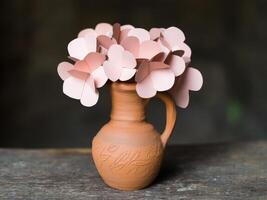 Paper flowers arranged in a handmade clay vase on an old wooden table, Crafted with care, gentle colors, and love in every petal. photo