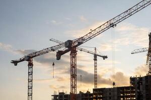 Cranes loom at a construction site against a colorful sunset, as workers engage in various tasks to progress the building project photo