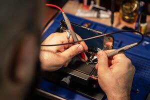 Technician repairing smartphone battery using soldering tools in a tech workshop during daylight hours photo