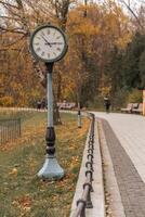 Classic clock stands tall in park surrounded by autumn leaves on a quiet afternoon photo