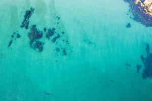 Top down view of sandy beach shoreline with rocks and transparent sea, drone view photo
