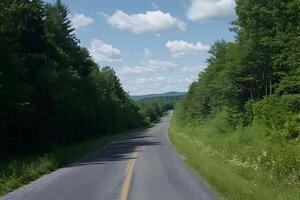 Wide empty asphalt road stretching into the distance, bordered by lush green trees under a blue sky photo