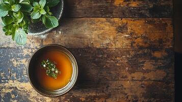 Aromatic Broth in a Rustic Bowl with Fresh Herbs. A top-down view of a flavorful soup garnished with fresh herbs, served in a dark bowl on a rustic wooden table. photo