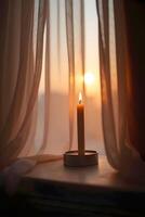warm, glowing candle sits on a windowsill beside sheer curtains gently swaying in the soft light of dusk or dawn filtering photo