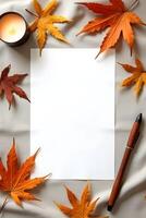Blank paper with autumn leaves, pen and a candle on a soft fabric background photo