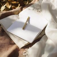blank notebook with white pages and gold pen rests on soft fabric, surrounded by autumn leaves, evoking sense of creativity and inspiration photo