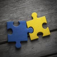 Two puzzle pieces, one blue and other yellow, connect on wooden surface, symbolizing unity and collaboration photo