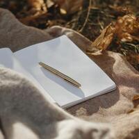blank notebook with gold pen rests on soft surface surrounded by autumn leaves, inviting creativity and reflection photo