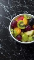 vibrant bowl of fresh fruit salad featuring mix of grapes, kiwi, and melon on sleek black marble surface photo