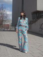 stylish woman in turquoise outfit with fish pattern, walking confidently on sunny day in urban setting photo