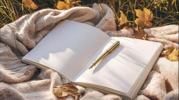 serene scene featuring open notebook with blank pages, golden pen resting on it, surrounded by autumn leaves and soft fabric photo