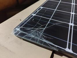 solar panel with cracked glass lies surface, showcasing damage and wear. sunlight reflects off broken surface, highlighting fragility of solar photo