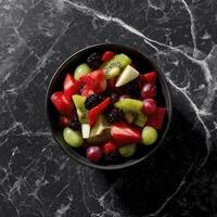 vibrant bowl of fresh fruit salad featuring strawberries, kiwi, grapes, and blackberries, beautifully arranged on black marble surface photo