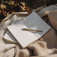 blank notebook with white pages and gold pen rests on soft fabric, surrounded by autumn leaves, inviting creativity and reflection photo