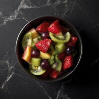 bowl of fresh fruit salad featuring strawberries, kiwi, grapes, and melon on black marble surface, evoking sense of freshness and vitality photo