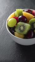 vibrant bowl of fresh fruit salad featuring mix of grapes, kiwi, pineapple, and melon, beautifully arranged on dark surface photo