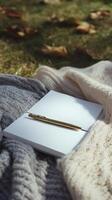 blank white notebook with gold pen placed on top, surrounded by cozy knitted blankets, evokes sense of calm and creativity photo