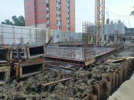 Construction site with foundation work, steel reinforcement, and building materials visible, showcasing urban development and progress photo