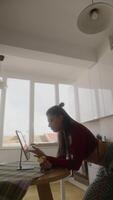 un enfocado joven mujer es trabajando atentamente y diligentemente a hogar mientras utilizando su ordenador portátil computadora video