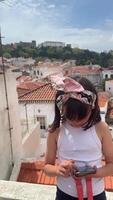 A young girl joyfully using a smartphone while seated on a rooftop, enjoying her summer afternoon video