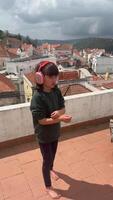 uma alegre criança danças em uma telhado com fones de ouvido, desfrutando vida dentro uma lindo configuração video