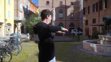 A young man wearing a black hoodie is gesturing expressively in a vibrant urban setting video