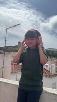 uma alegre criança quem é alegremente desfrutando música em uma telhado enquanto vestindo fones de ouvido entusiasticamente video