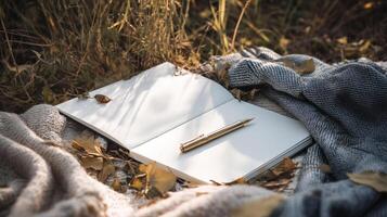 serene scene featuring open notebook with blank pages resting on cozy blanket surrounded by autumn leaves. golden pen adds touch of elegance photo