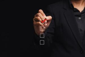 Businessman holding a pen and checking a mark on the boxes symbol is one of four options while standing on a black background photo