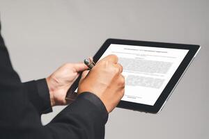Businessman an electronic signature on a tablet while standing on a gray background in the office photo